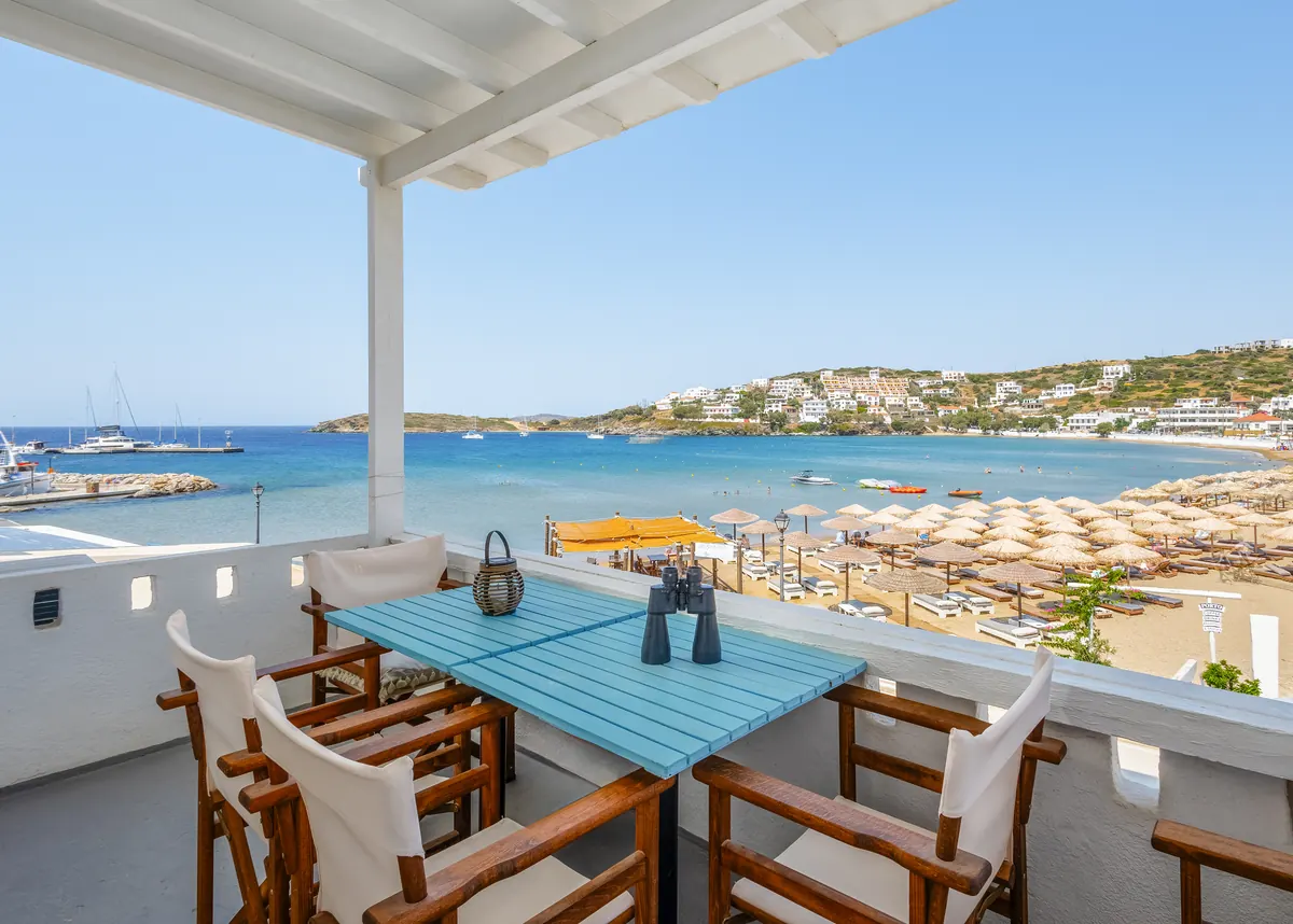 Überdachte Terrasse der Ferienwohnung mit blauem Tisch und Holzstühlen, mit Blick auf den Strand von Batsi